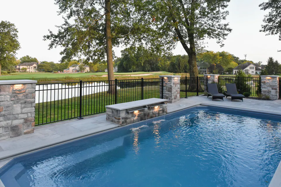 Pool edge with stone bench wall, piers, fence, lawn, and pond view beyond